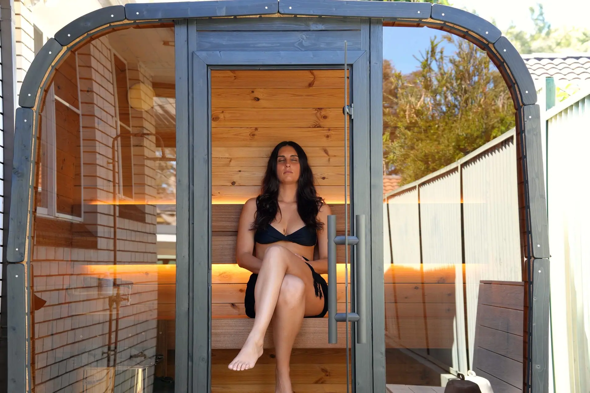 The curved Koda sauna front and glass panels with Mia seated inside at Mortdale