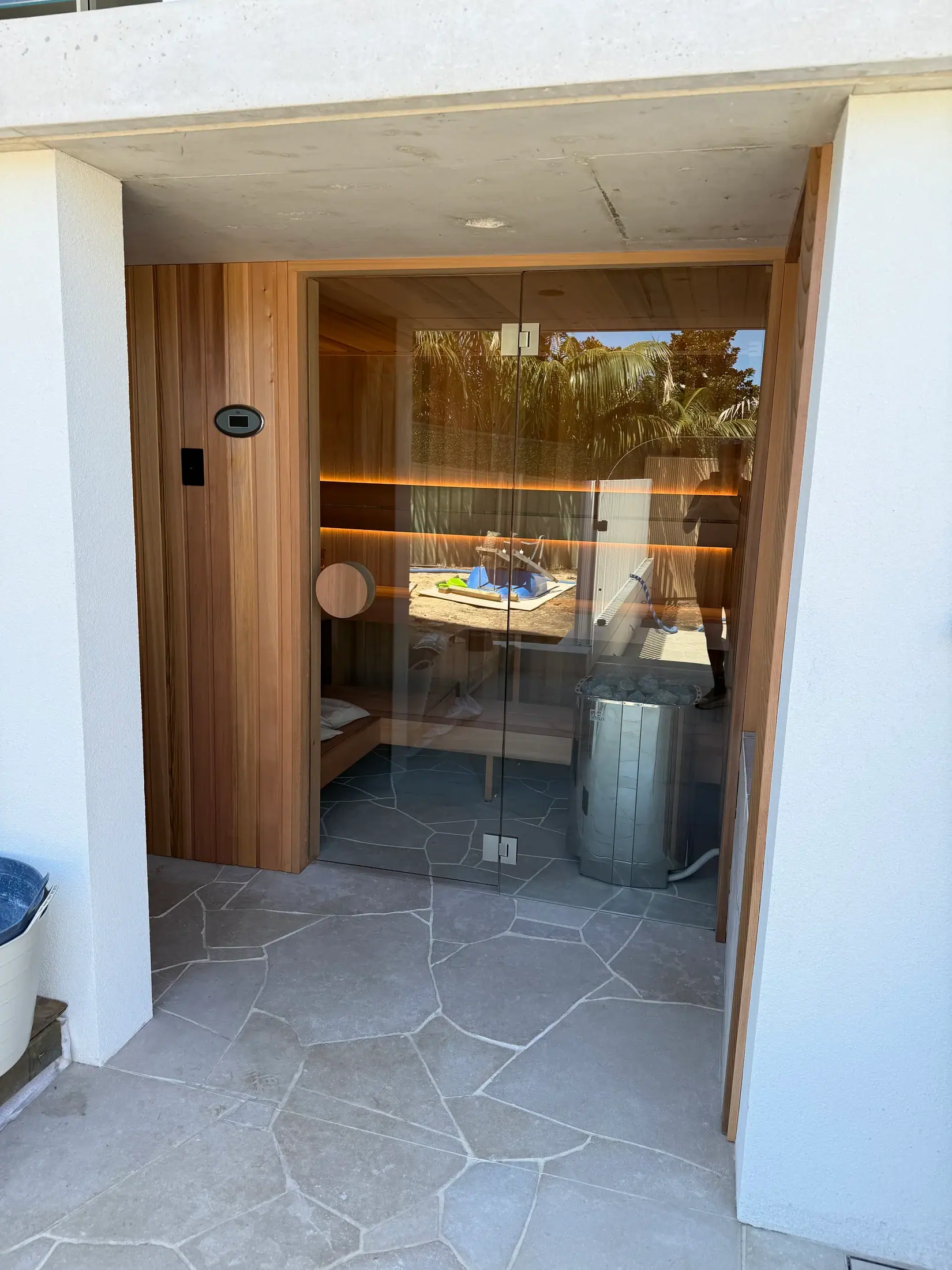 Courtyard sauna with wide glass front, stone floor and illuminated cedar seating